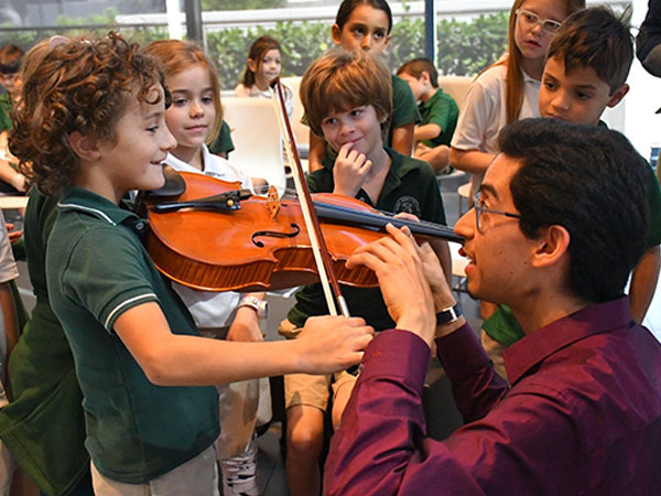 young boy holding a violin receiving instructions on playing from an icopr player