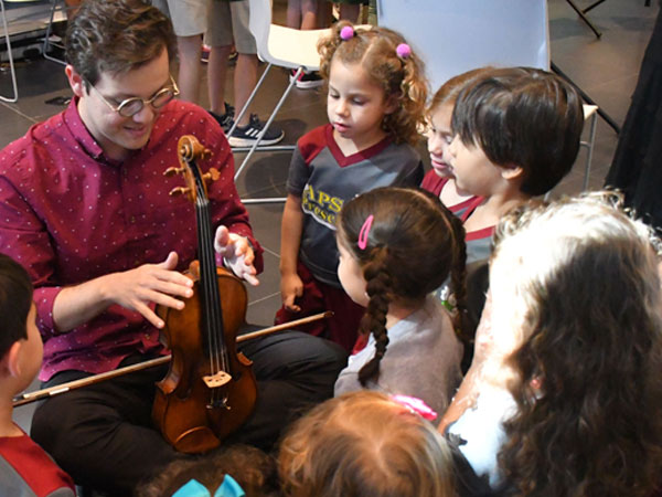children gathered around an icopr player learning about the violin
